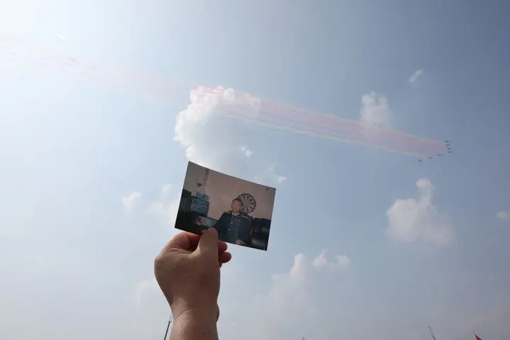 2025年9月3日,空中梯队飞过天安门广场时,王伟烈士的妻子阮国琴在观礼台上把王伟的照片举向蓝天。新华社记者 殷刚 摄
