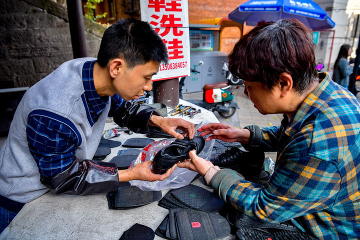 4月19日，重庆市九龙坡区谢家湾街道民主村社区居民（右）来到“小黄皮鞋匠”修鞋。