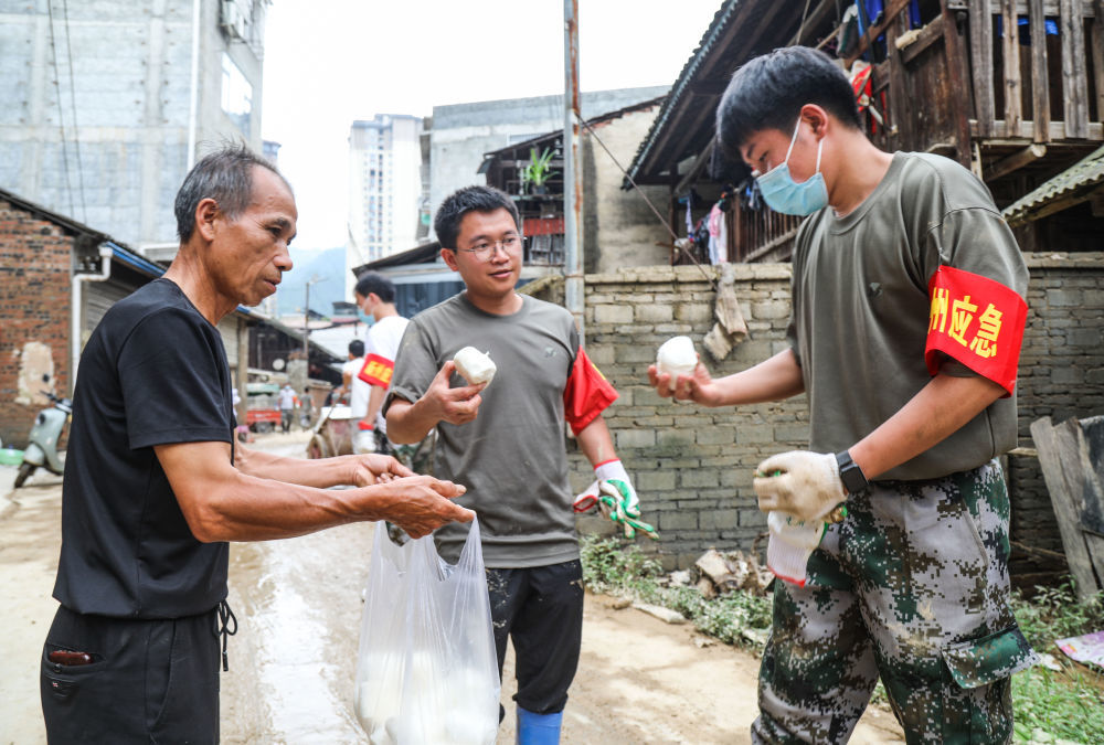 ↑6月27日,村民(左)把蒸好的馒头送到救援人员手中。
