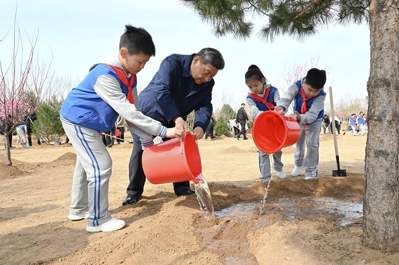 △2025年4月3日，习近平总书记来到北京丰台区永定河畔参加首都义务植树活动。这是总书记同少先队员一起给刚栽下的树苗浇水。