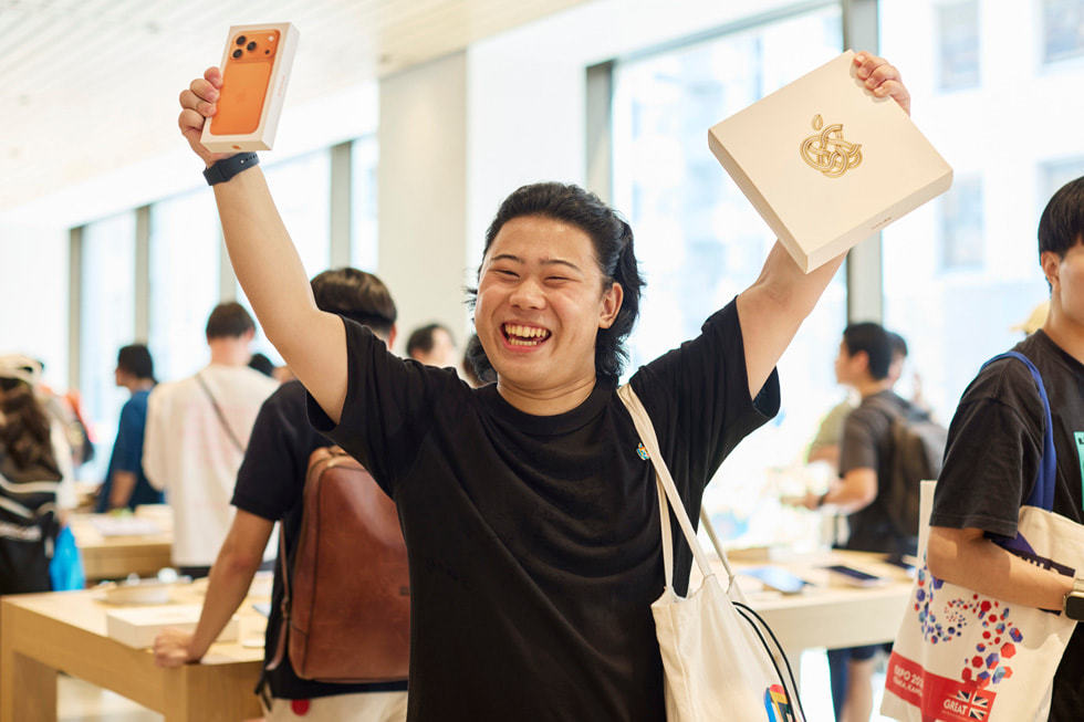 一位顾客一手拿着星宇橙色 iPhone 17 Pro，一手拿着 Apple 银座零售店纪念品。