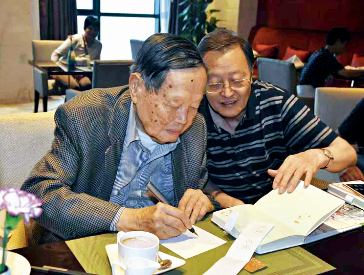 ·2018年,杨振宁(左)回合肥工作,抽空与亲人见面。图中的他正要为杨振和带来的照片题字留念。(杨振和供图)