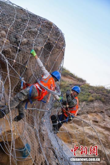 图为兰州铁路局兰州西工务段两名铁路职工密切配合在山体上铺设柔性主动钢丝大网 王光辉 摄