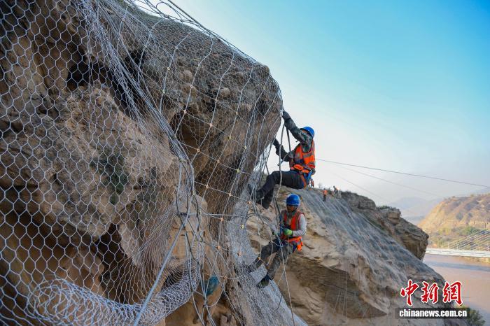 11月上旬,甘肃省兰州市西固区境内的兰新铁路西固城至坡底下区间的陡峭山体上,兰州铁路局兰州西工务段的工作人员攀爬在近百米高、看似直立的石质山体上,为山体加装柔性主被动防护钢丝网。北方汛期结束后,兰州西工务段加大兰新、兰青、包兰铁路沿线陡峭山体、危岩落石地段的排查整治,按照轻重缓急,在陡峭山体、隧道口等重点地段,通过加装柔性主被动防护钢丝网和搜山扫石的方式,有效防止风化落石、活石、浮石等掉落到铁路线路上。在太阳的照射下,柔性钢丝网闪着银光,远远望去,犹如电影里刀枪不入的“金丝软甲”,包裹在整个峭壁裸露在外面的山体岩石上,为过往列车构筑起一道坚固的安全屏障。王光辉 摄