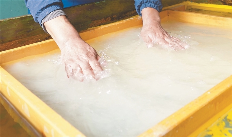 图为阿旺曲央用双手抚平纸浆附帘，使纸浆紧密贴合勾勒平整基底。