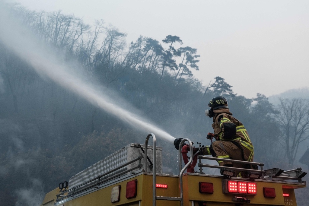 当地时间2025年3月26日，韩国庆尚北道义城郡，消防员使用消防车上的水炮扑灭在孤云寺火灾中烧毁大部分建筑后残留的火焰。视觉中国 图