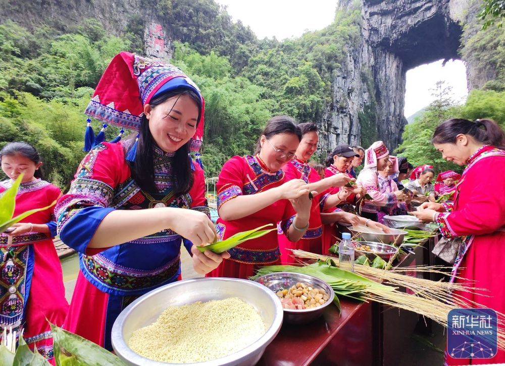 ↑ 5月23日，在广西罗城仫佬族自治县怀群镇天门山景区，游客与村民在参加包粽子比赛。新华社发（蒙增师摄）