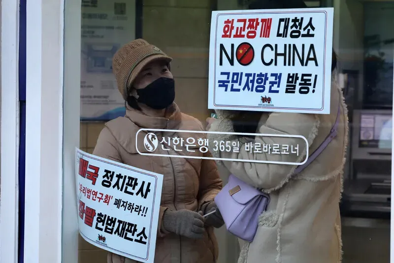 2025年2月10日,两名反弹劾集会参与者站在首尔钟路区韩国宪法法院附近的一家银行的 ATM 机内,银行的窗户上靠着标语。尹锡烈的弹劾审判正在此举行听证会。