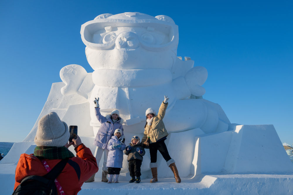 ↑1月3日，在哈尔滨冰雪大世界园区，游客与亚冬会吉祥物雪雕“滨滨”合影。新华社记者 张涛 摄