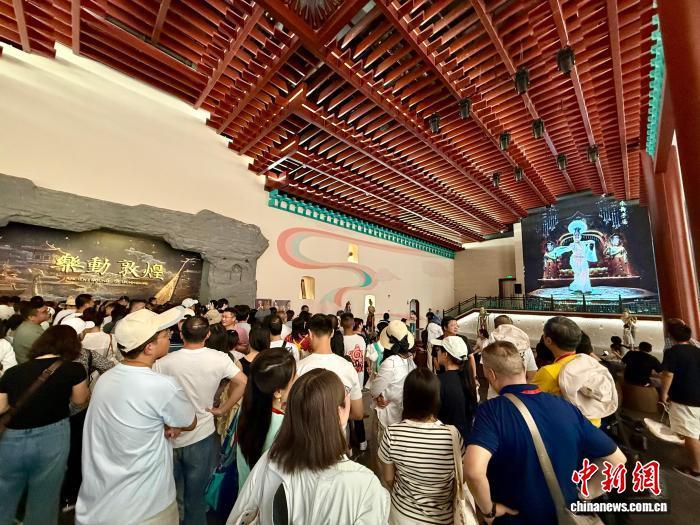暑期来临,甘肃省敦煌市旅游高峰也随之到来,由甘肃演艺集团打造的全球首部洞窟式沉浸体验剧《乐动敦煌》近期吸引众多游客前往观看。该剧讲述了西域少年白歆苦苦追寻并最终在敦煌乐舞壁画中领略到音乐真谛的故事,以可看、可听、可游走、可互动的沉浸式体验形式,为观众再现敦煌音乐、舞蹈、诗歌、壁画等敦煌盛景画卷,全面展现敦煌传承发展了千百年的古乐文化魅力,被誉为莫高窟“活的”第736窟。图为开场前,游客等候观影时观看动画观影指南。王牧雨 摄