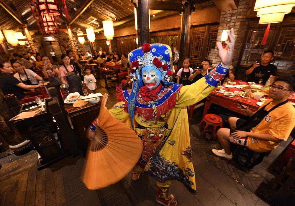 图为食客在四川省成都市宽窄巷子景区内的一家火锅店观看“变脸”表演。新华社记者 刘坤 摄