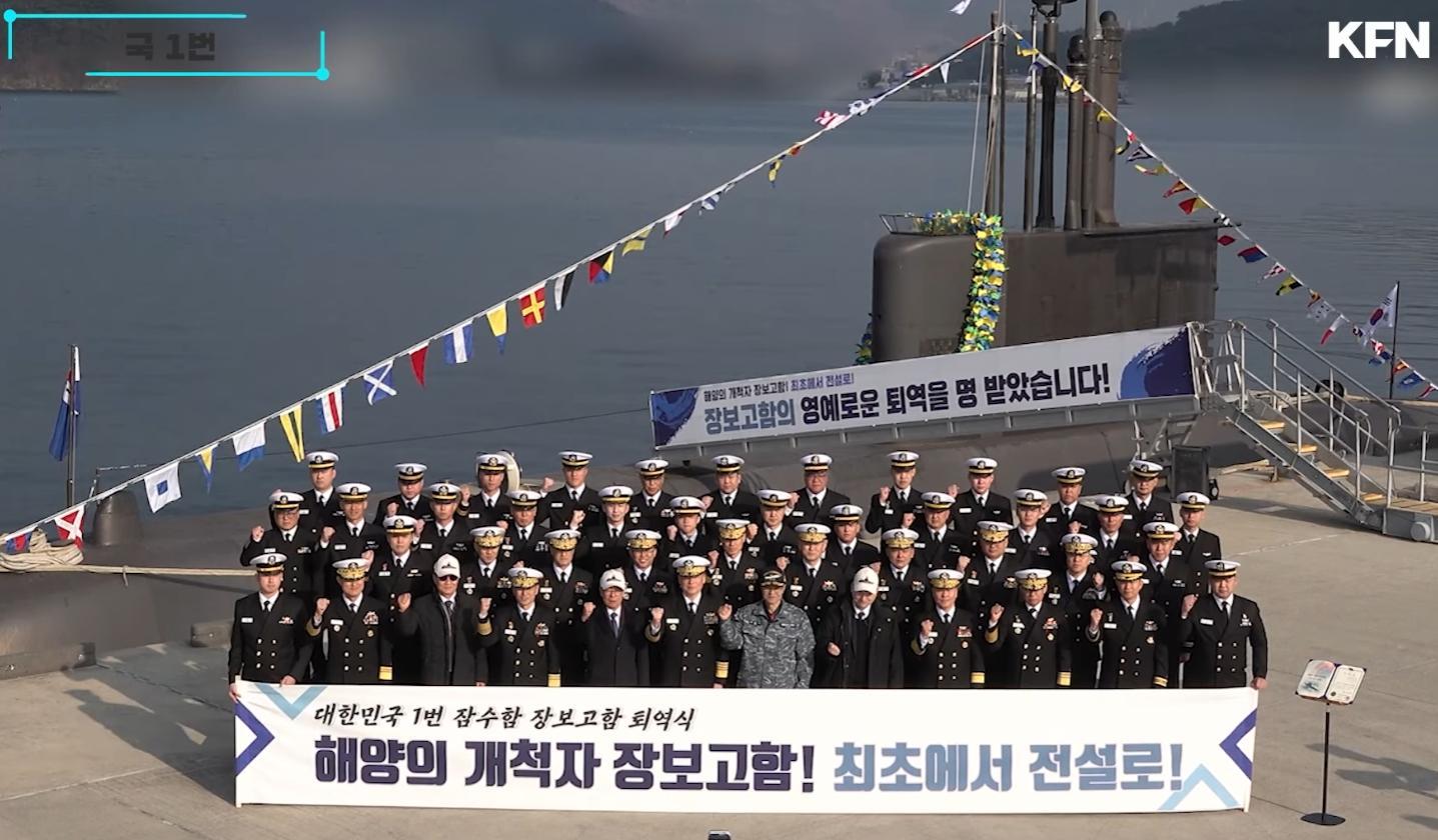 横幅上的谚文意为：“大韩民国1号潜水舰张保皋号退役仪式 海洋的开拓者张保皋号！从第一艘驶向传奇！”舷梯上的谚文意为“海洋的开拓者张保皋号！从第一艘驶向传奇！张保皋号已获准光荣退役”