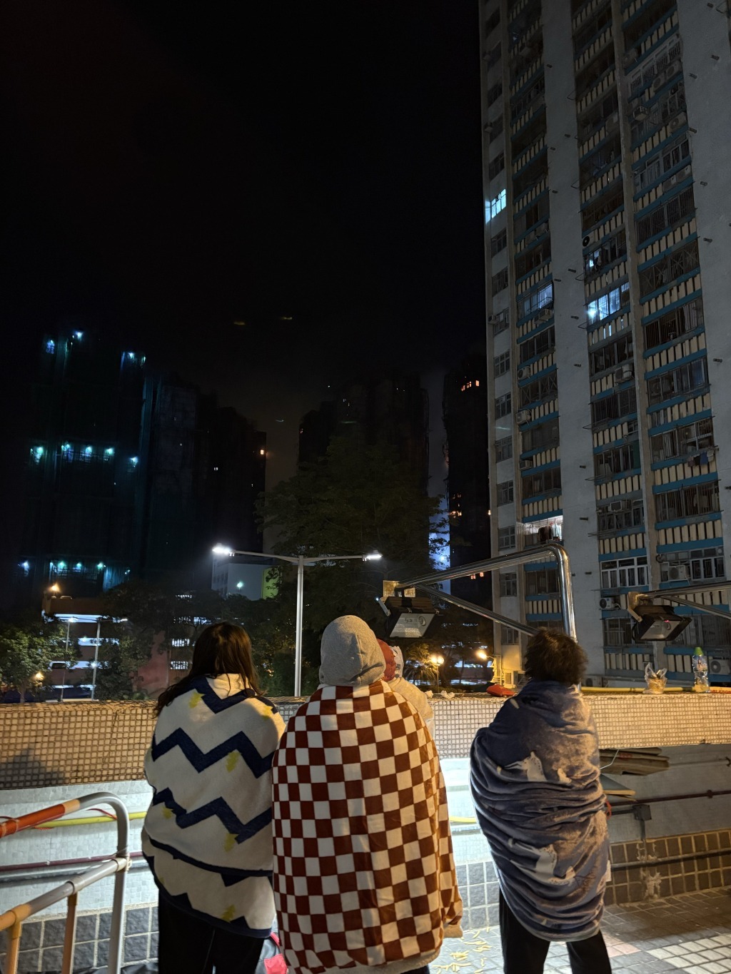 广福商场二楼露天广场,被疏散居民裹着毛毯观望火势