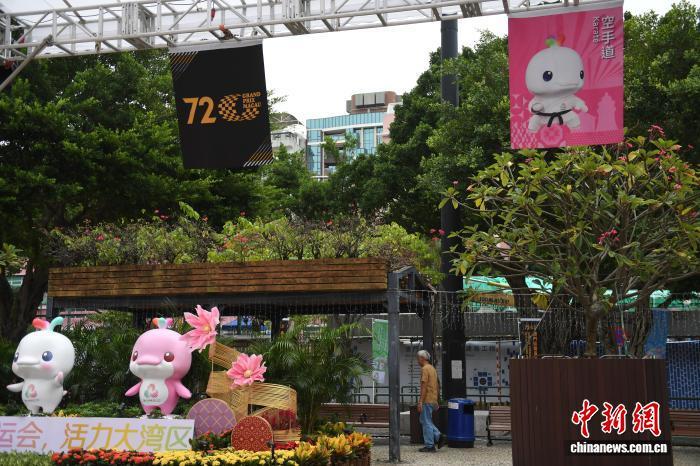 2025年11月6日，随着第十五届全国运动会(简称“十五运会”)开幕进入最后3天倒计时，澳门赛区迎接十五运会开幕的氛围浓厚。图为塔石广场上的十五运会吉祥物“喜洋洋”“乐融融”雕塑以及十五运会和第72届格兰披治大赛车宣传彩旗飘扬。　中新社记者 郑嘉伟 摄