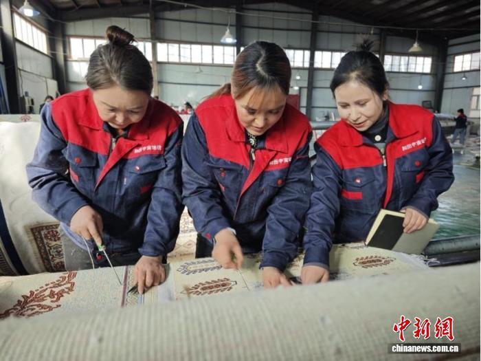 阿尔孜古丽(右一)在生产线上查看地毯编织流程工艺。闫兆霞 摄