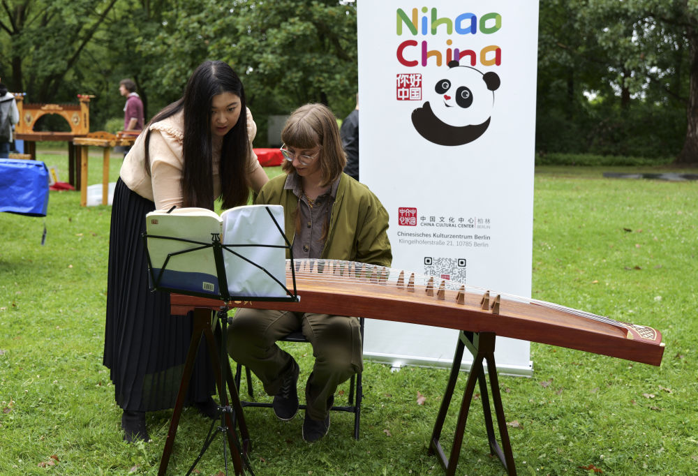 7月12日，在德国首都柏林的世界公园，一名参观者在中国展区学习弹奏古筝。新华社记者 顾梓峄 摄