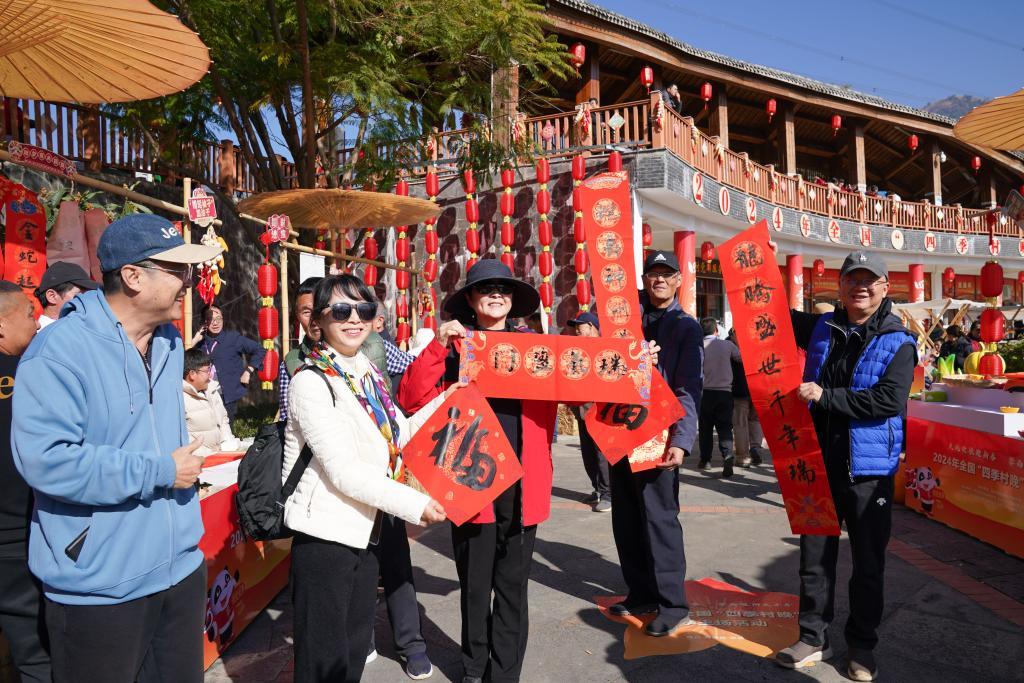 2024年全国“四季村晚”冬季主场活动在四川攀枝花市米易县龙华村举行，游客在乡村年货大集上展示春联。新华社记者 胥冰洁 摄