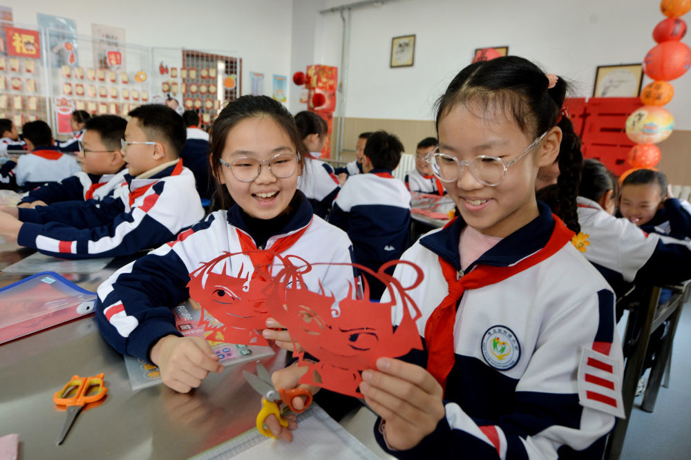 2月14日，两名学生在山东青岛宜阳路小学“传统文化润童心”主题活动中学习“哪吒”剪纸。当日，多地中小学开学，迎来春季新学期。新华社发（王海滨 摄）