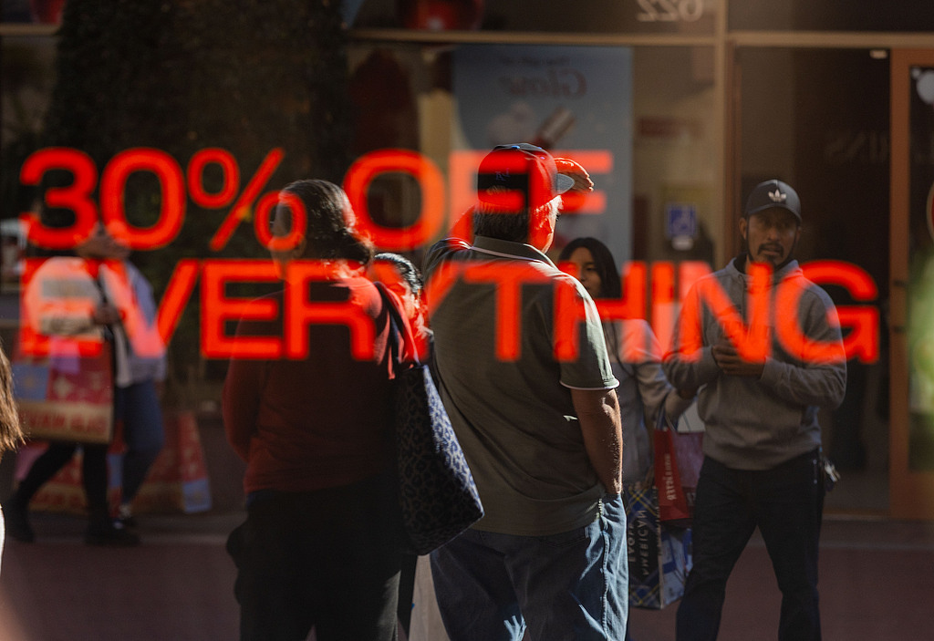 美国加利福尼亚州科默斯,顾客穿过城堡奥特莱斯,一家商店外打出促销广告。(视觉中国)