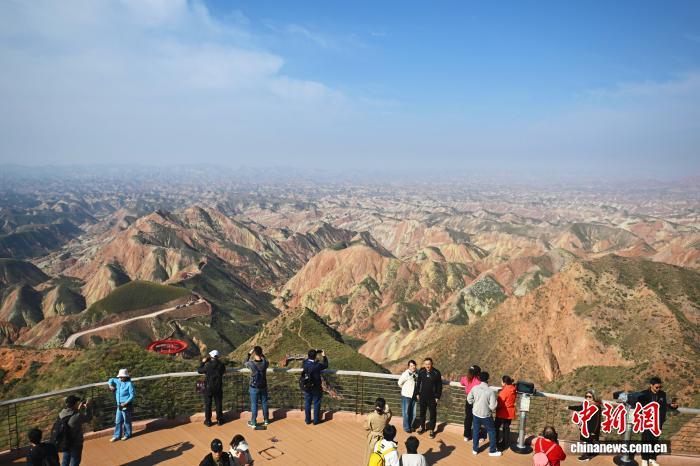 10月19日，“兰州国际传播交流宣传周”联动融合采访活动在甘肃兰州启动，来自加拿大、新西兰、韩国、德国、爱尔兰、马达加斯加等国家和地区的海外华文媒体代表走进兰州水墨丹霞景区感受1.5亿年前的地质奇观。据了解，该景区总面积400平方公里，是目前中国已发现面积最大的同类型地貌景观，距今约有一亿五千万年的历史，主要以红山湾地貌为主，兼有丹霞崖壁、孤峰、幽谷、一线天、风动石等奇特景观，山体瑰丽多姿犹如山水泼墨画。图为融合采访团成员与游客一起拍摄参观兰州水墨丹霞。中新社记者　李亚龙　摄