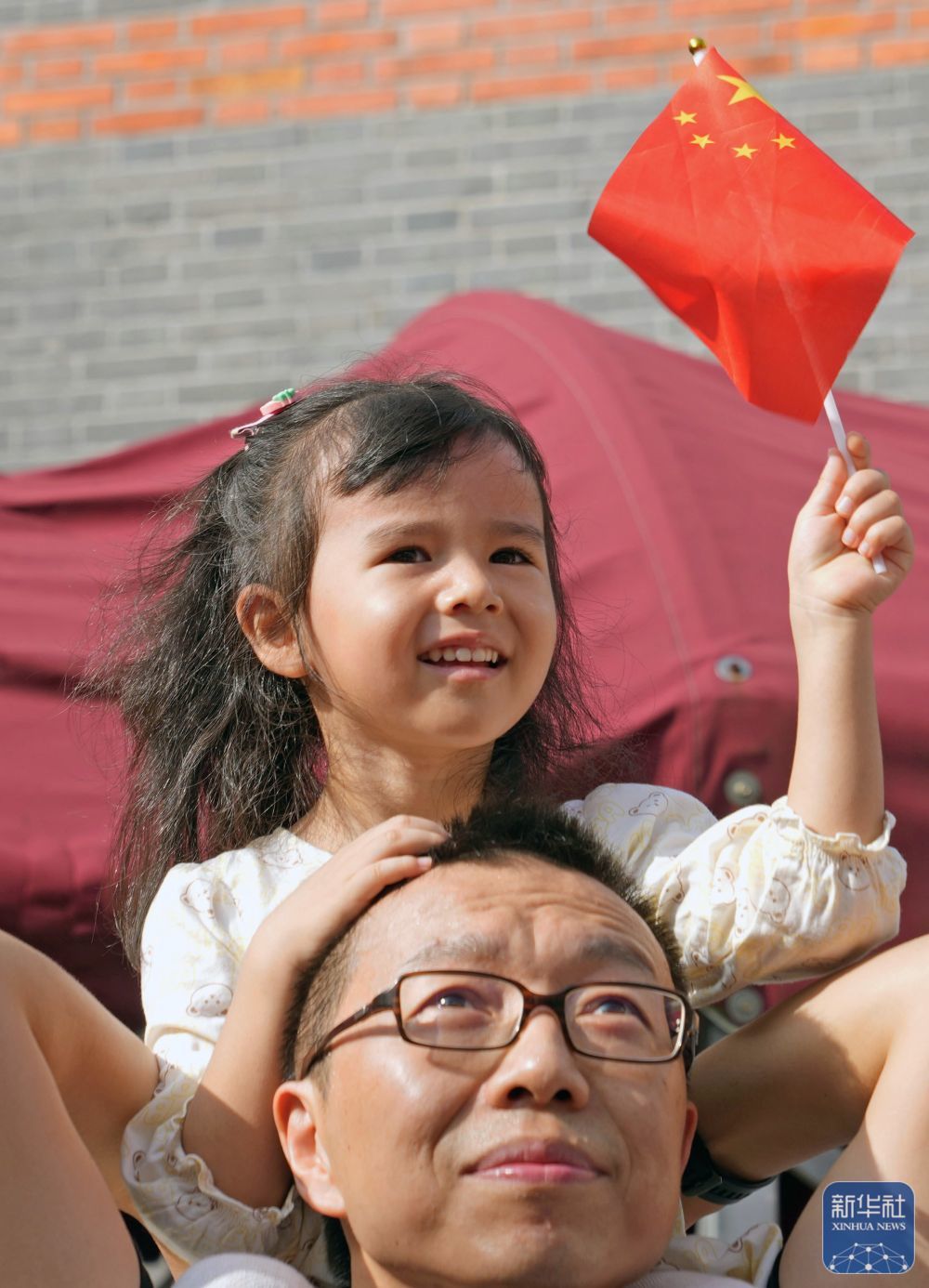 ↑ 10月1日,在上海中共一大纪念馆,一名小女孩坐在爸爸的肩膀上观看升旗。新华社记者 刘颖 摄
