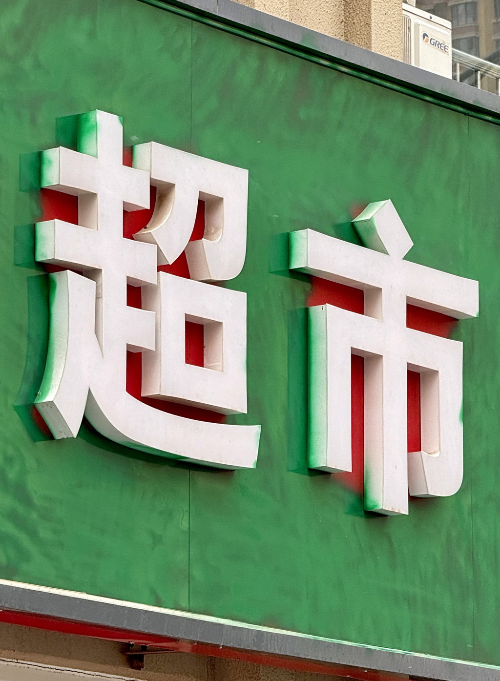 一家超市的门头底色直接被刷成绿色，仔细看，字体间不容易刷到的地方，红色还清晰存在。崔朋克 图