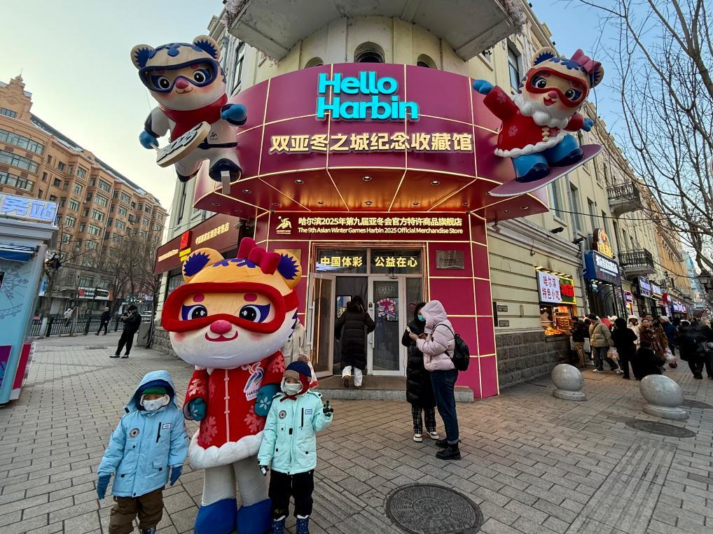 位于哈尔滨中央大街的亚冬会特许商品零售店门前，游客与吉祥物“妮妮”合影。新华社记者 杨思琪 摄