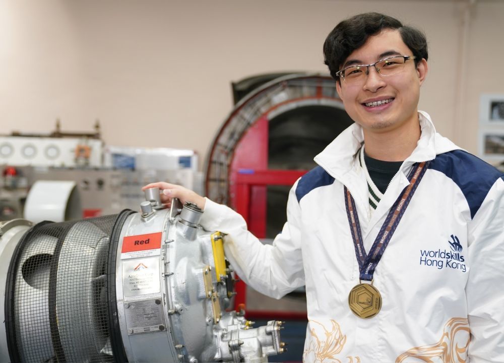 在香港专业教育学院,黄富东佩戴着“2024年里昂世界技能大赛”飞机维修项目的铜牌和涡轮螺旋桨飞机引擎合影(1月14日摄)。新华社发(王申摄)