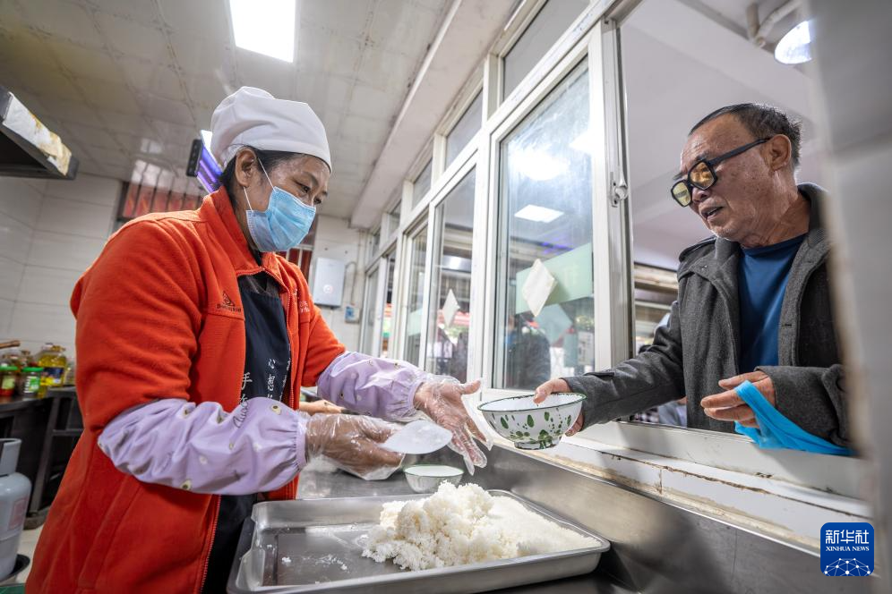 在昆明市幸福家园小区爱心食堂,王兰兰给一名老人打饭(5月28日摄)。