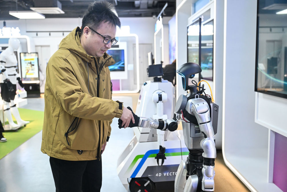 2025年12月4日,在南京人工智能生态街区的“AI·模坊”南京智能体集散中心,工作人员与机器人握手。新华社记者 季春鹏 摄