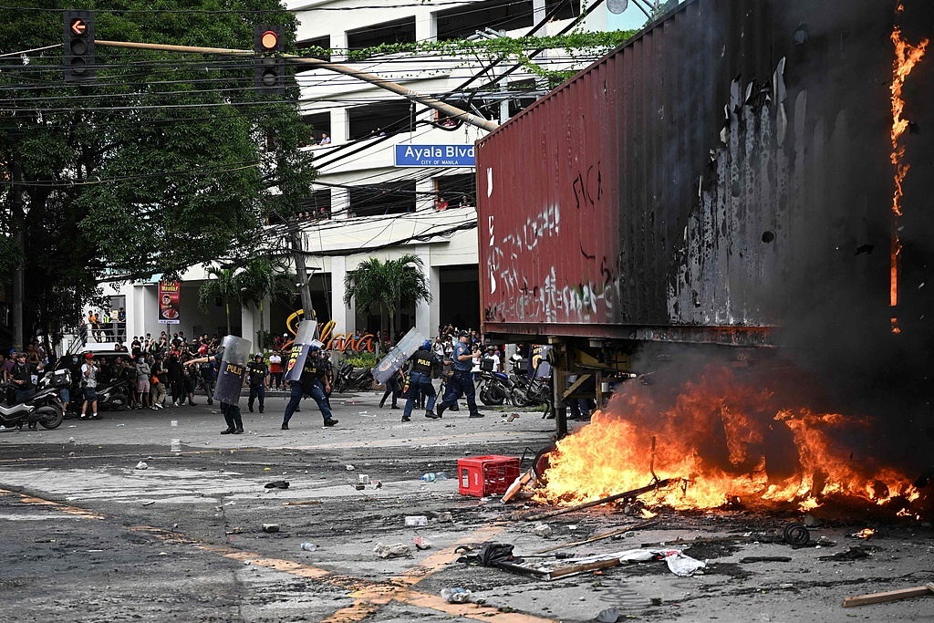 21日，菲律宾全国爆发反腐抗议活动。图为一群青年焚烧拖车后向警察投掷石块，警察举盾牌防御。（视觉中国）