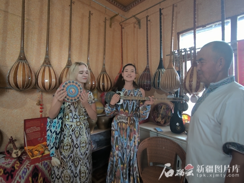 7月28日，在新和县依其艾日克镇加依村，俄罗斯籍网络达人梅丽莎（左）和网络名人古丽皮亚·买买提依明（中）正在体验民间手工乐器。石榴云/新疆日报记者 甘兴华摄
