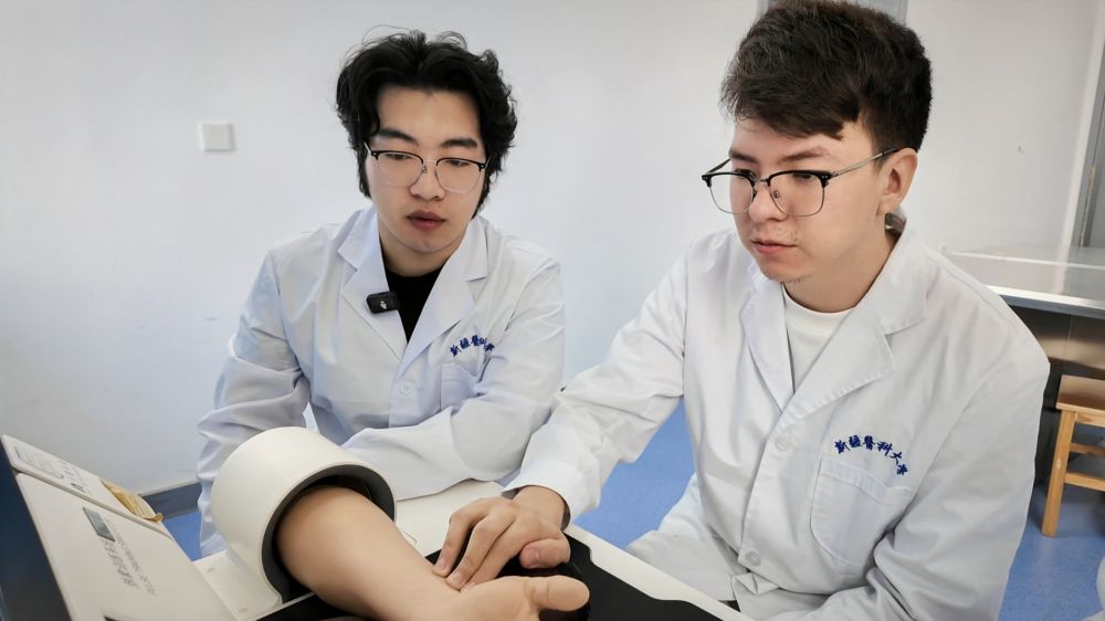5月9日，卡力别克&middot;叶尔波森（右）在新疆医科大学使用脉象模拟仪器练习脉诊（手机照片）。新华社记者 王泽宇 摄