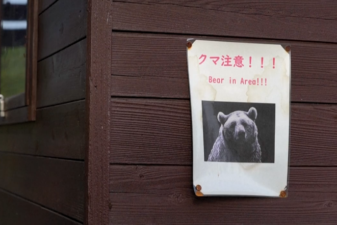 2025年10月25日，外媒电视台拍摄的视频画面显示，秋田县一片森林附近贴着一张“注意熊出没”的警告标志/图源：广州日报