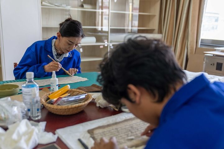 西藏自治区古籍保护中心古籍修复员次仁央宗（左）与同事对古籍进行除霉（2025年8月13日摄）。新华社记者 晋美多吉 摄