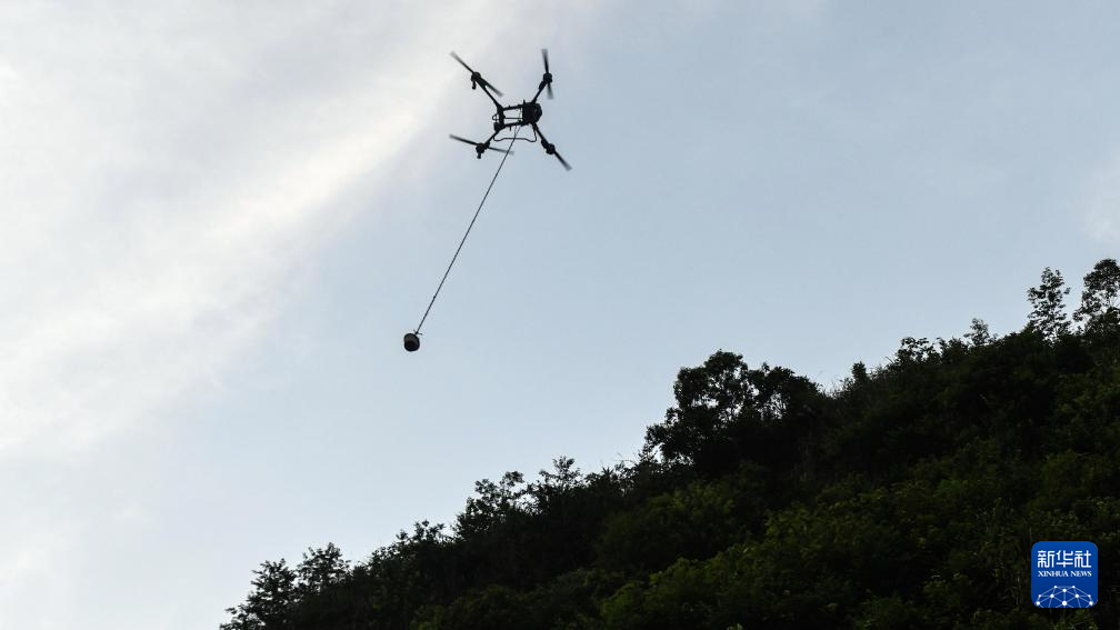 桥隧工人遥控无人机给隧道山体上的施工点运送混凝土（7月15日摄）。