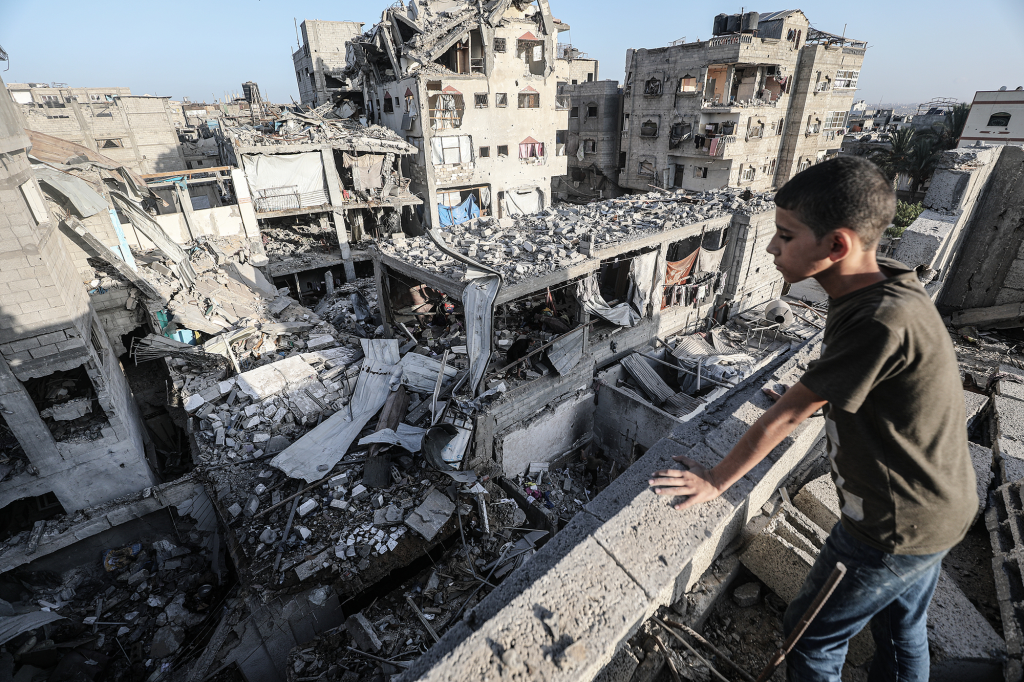 2025年10月20日,加沙布赖杰,一名儿童望向布赖杰难民营内被摧毁的建筑。尽管加沙地带已达成停火协议,但以色列仍对该地区发动袭击,造成多人死伤。视觉中国 图