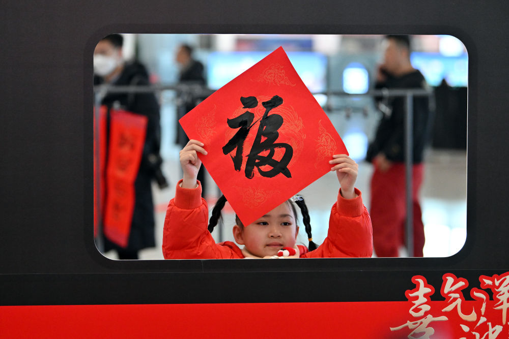 1月14日，在太原南站，一名小乘客拿着福字在候车大厅拍照留影。新华社记者 詹彦 摄