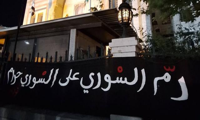 叙利亚抗议者在大马士革人民议会大楼上挂出反战标语。
