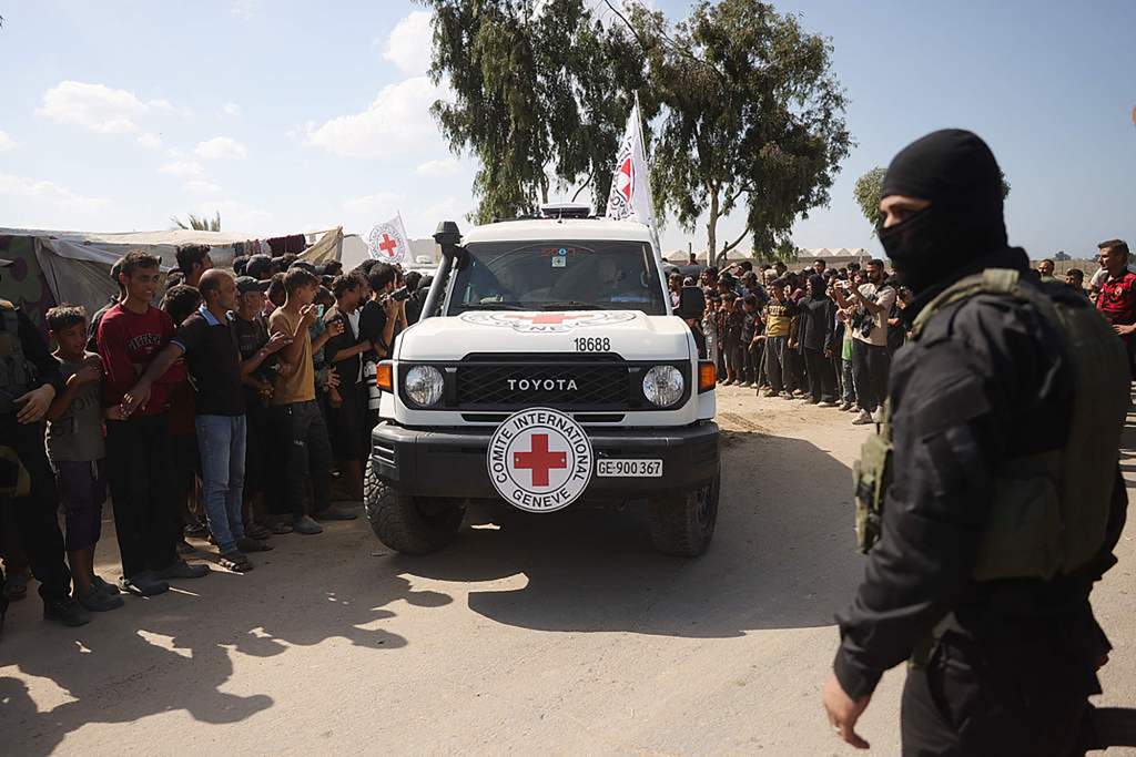 2025年10月13日,加沙地带中部代尔巴拉赫南部,一名哈马斯下属武装派别卡桑旅武装分子站岗,一群巴勒斯坦人围观红十字国际委员会(ICRC)的车辆载着被释放的以色列人质离开。视觉中国 资料图