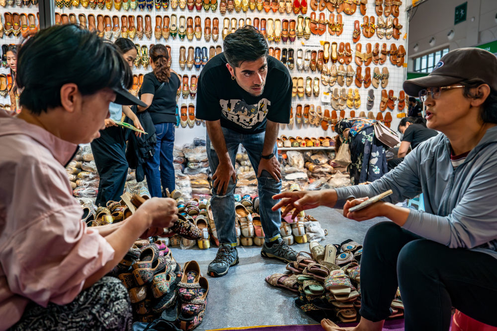 6月21日，第9届中国—南亚博览会南亚馆巴基斯坦展区的参展商（中）向观众推介手工拖鞋。