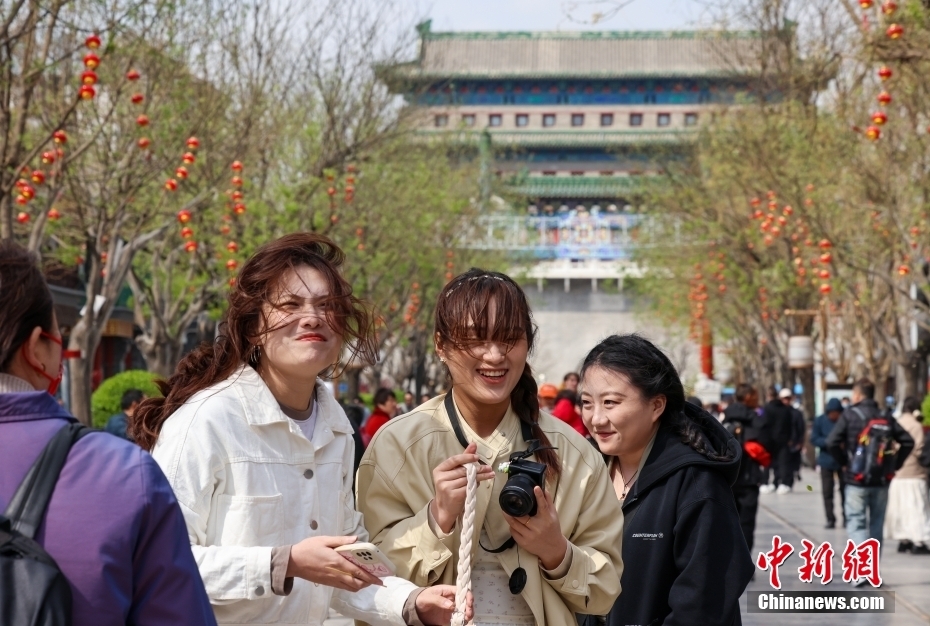 4月12日，游客在北京前门大街游览时遇到强风转身躲避。当日，北京大风橙色预警信号持续生效，6时至22时为风力最强时段。中新社记者 张宇 摄