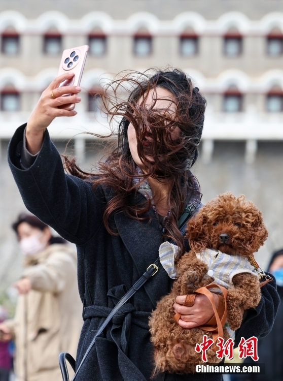 4月12日，游客携爱犬在北京前门大街自拍。当日，北京大风橙色预警信号持续生效，6时至22时为风力最强时段。中新社记者 张宇 摄