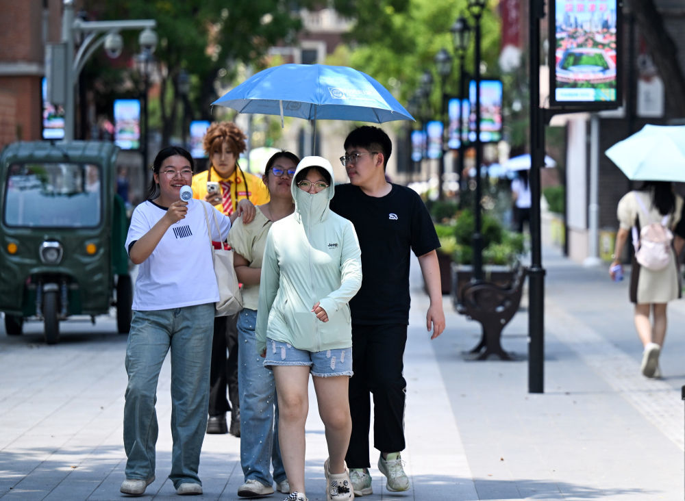 在天津市五大道文化旅游区，游客用遮阳伞、小风扇等降温防晒。新华社记者 赵子硕 摄