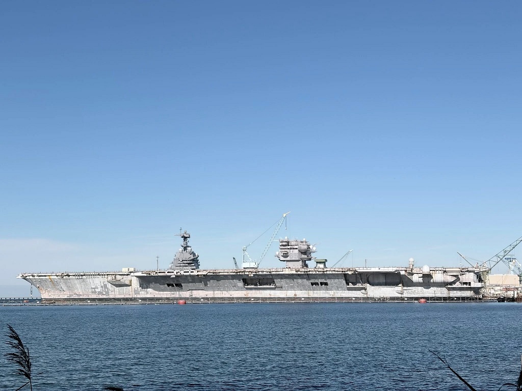 一张拍摄于纽波特纽斯造船厂舾装码头的照片,前景处的舰体以及右侧已拆除桅杆的舰岛为已经退役等待拆解的CVN-65“企业”号,左侧舰岛则属于舰体被“企业”号遮挡的CVN-79“约翰·F·肯尼迪”号