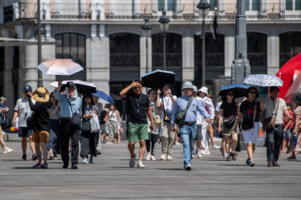 当地时间2025年7月17日,西班牙马德里,游客在太阳门进行徒步游并用阳伞遮阳。