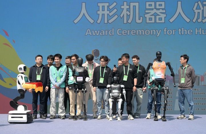2025年4月19日，一台机器人在人形机器人颁奖仪式上托举着奖牌走向获奖机器人选手和技术团队。当日，2025北京亦庄半程马拉松暨人形机器人半程马拉松举行。新华社记者 李贺 摄