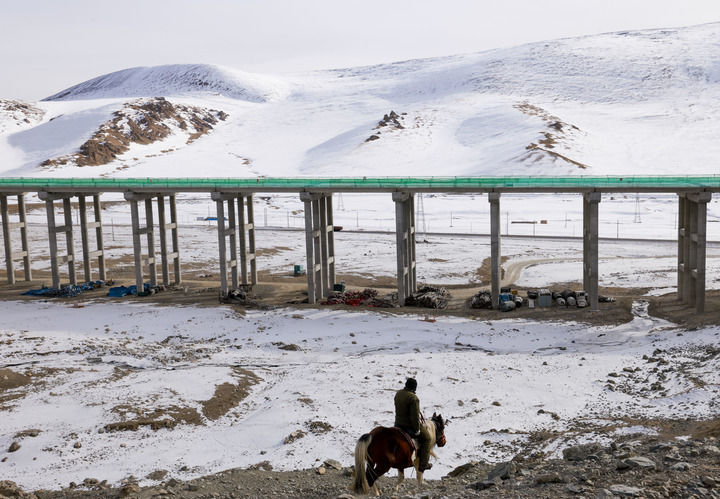 2024年12月30日，在新疆和静县，牧民骑马从在建的新疆乌尉（乌鲁木齐至尉犁）高速公路附近经过。新华社记者 王菲 摄