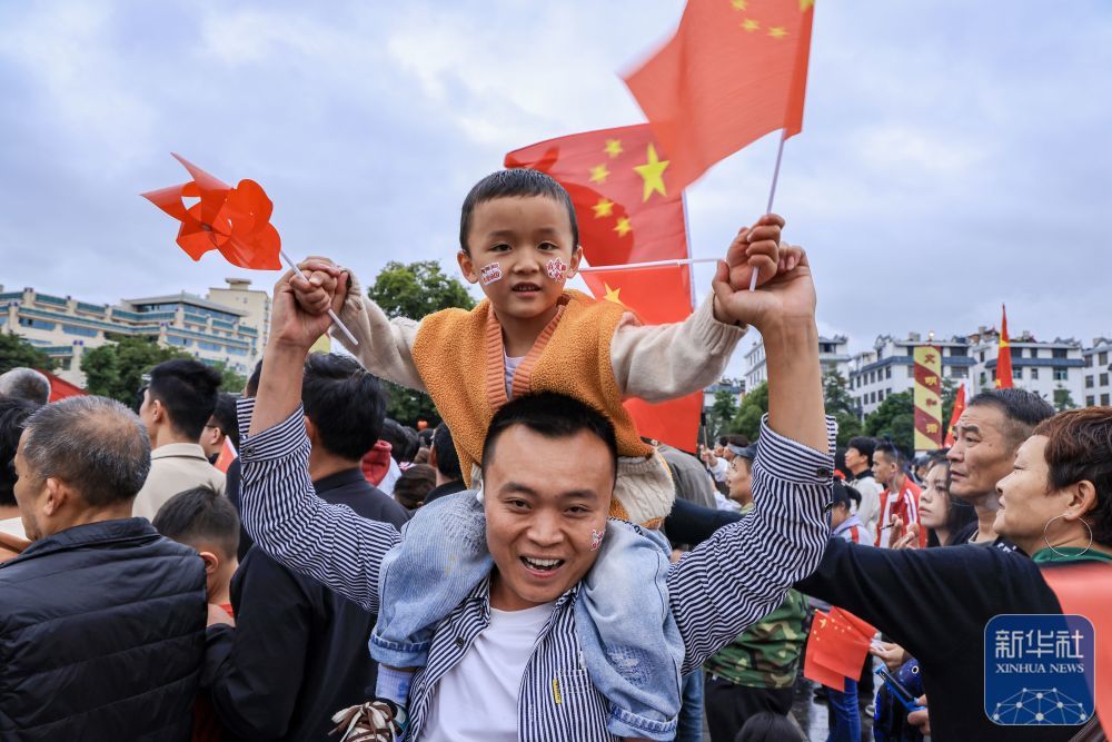 ↑ 10月1日,一对父子在云南省曲靖市麒麟区南城门广场观看升旗。新华社发(孙文来摄)