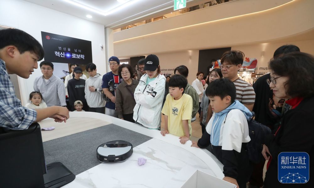 ↑2025年10月12日，在韩国首尔近郊的一家大型购物中心，韩国消费者观看中国品牌扫地机器人演示。